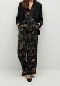 Conjunto de seda negra con estampado que incluye una camisa de botón y pantalones de pierna ancha, decorados con diseños florales y arquitectónicos en dorado.