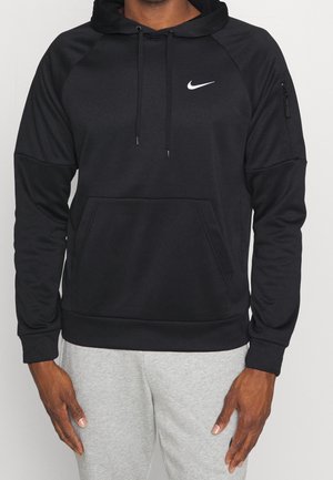 Mand iført sort Nike hættetrøje med frontlomme og lynlåslomme på ærmet, kombineret med lysegrå joggingbukser.