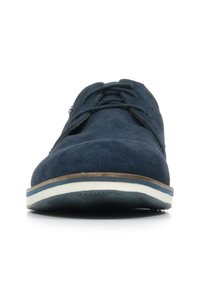 Marineblauwe suède schoen met een ronde neus, gesloten vetersluiting en een witte tussenzool met een blauwe streep. Gestructuurd bovenwerk met minimale hardwareaccenten.