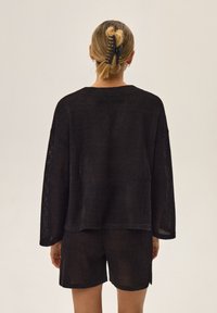Czarny zestaw składający się z dzianinowej bluzki z siateczki i szortów, z długimi rękawami, luźnym krojem i bocznymi rozcięciami. Gładka tekstura z swobodnym fasonem.