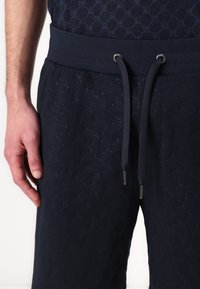 Pantalones de chándal navy con un patrón texturizado, cintura elástica y cordón. Presenta acentos metálicos en los extremos del cordón.