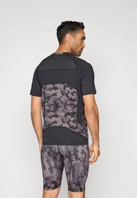 Lühikeste varrukatega sportlik särk, millel on must ülaosa ja hall kamuflaaživoodriga seljaosa; sobitatud samasuguste hallide kamuflaazimustriliste lühikeste pükstega.