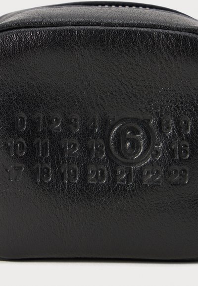 Schwarze Lederhülle mit strukturierter Oberfläche, die geprägte Zahlen und ein kreisförmiges Design aufweist. Reißverschluss oben.