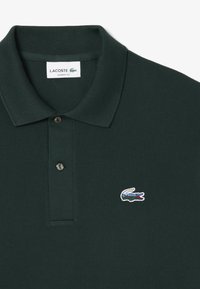 Donkergroene polo shirt gemaakt van gestructureerde stof. Heeft een klassieke kraag, een knoopsluiting met twee knopen en een geborduurd krokodillenlogo op de borst.