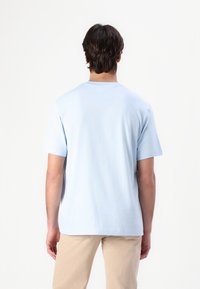 Tricou din bumbac de culoare albastră deschisă, cu mâneci scurte, decolteu rotund, croială lejeră și o textură fină, văzut din spate.