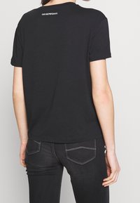 Černé bavlněné tričko s krátkými rukávy, kulatým výstřihem a malým bílým logem na horní části zad. Nosit s tmavými džíny.