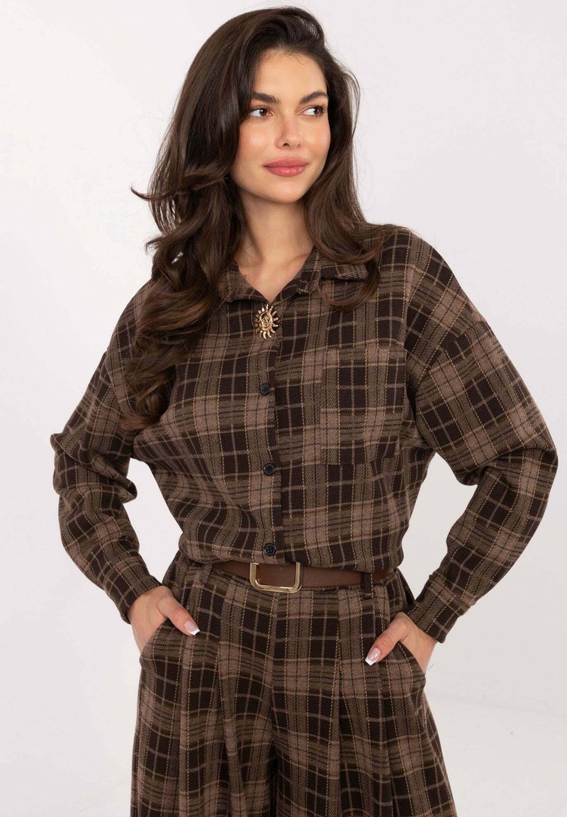 Brown plaid button-up shirt with long sleeves, featuring a collar and a decorative brooch. Paired with high-waisted, pleated trousers.