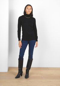 Un pull col roulé noir associé à un jean bleu foncé et des bottes en cuir noir hautes jusqu'aux genoux. Design simple avec une silhouette ajustée.