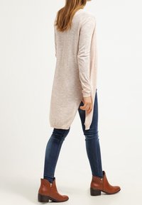 Dlouhý světle růžový svetr s ribovanými manžetami, bočními rozparky a volným střihem, spárovaný s tmavě modrými skinny džíny a hnědými kotníkovými botami.