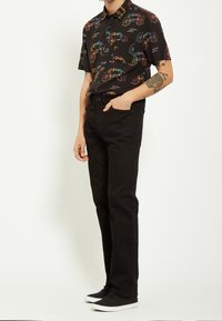 Chemise noire à manches courtes avec des motifs colorés d'animaux et d'éclairs, associée à un jean noir à jambes droites et des baskets noires.