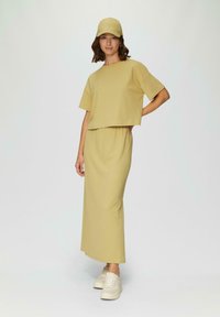 Lichtgele, gestructureerde tweedelige outfit bestaande uit een cropped top en een lange rok. Gecombineerd met een bijpassende pet en lichtgekleurde sneakers.