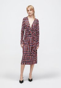 Vestido envelope com um padrão geométrico colorido em vermelho, azul e branco. Mangas longas, cintura com laço e comprimento até ao joelho. Tecido suave.