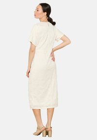 White knee-length dress with short sleeves, floral texture, keyhole back detail, paired with light-colored block-heel sandals.