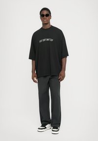 Black oversized t-shirt with white lettering, paired with dark pants and black and white sneakers. Accessorized with dark sunglasses.