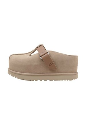 Zoccoli in suede beige con una fascia e dettagli in argento, dotati di una spessa suola in gomma e punta arrotondata, progettati per comfort e facilità d'uso.