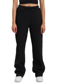 Black ribbed joggers with an elastic waistband, drawstring tie, and loose-fit design. Paired with white sneakers.