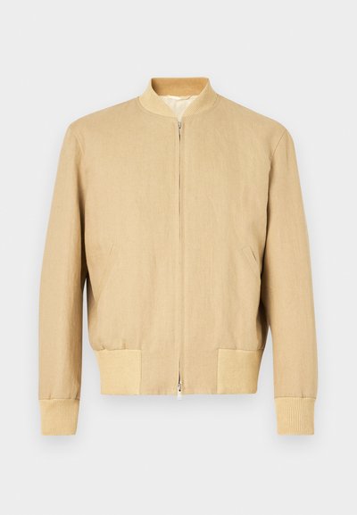 Bežs bomberis, kas izgatavots no viegla auduma, ar rāvējslēdzēja aizdari, ribota apkakle, aproces un divas sānu kabatas. Gluda tekstūra.