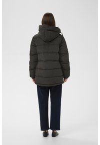 Czarna pikowana kurtka puchowa z kapturem, z poziomymi przeszyciami, o luźnym kroju, w zestawie z kontrastującymi ciemnoniebieskimi szerokimi spodniami.