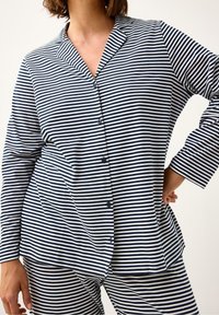 Set di pigiama a righe con una camicia con bottoni e colletto, realizzato in un morbido tessuto a righe blu navy e bianche. I pantaloni abbinano il design della camicia.