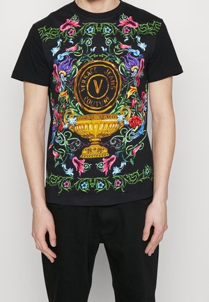 Czarny t-shirt z kolorowymi kwiatowymi i winoroślowymi wzorami otaczającymi złoty wazon i emblemat „Versace Jeans Couture” na piersi.