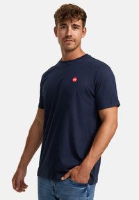 Camiseta de algodón azul marino con cuello redondo, mangas cortas y un pequeño logotipo rojo en el pecho. Ajuste casual y textura suave.