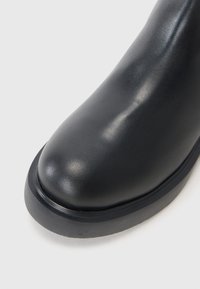 Juoda odinė batas su apvalia nosimi, glotnia tekstūra ir storu guminiu padu. Dizainas elegantiškas, su minimaliu detalizavimu.
