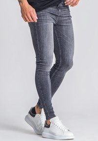 Jeans ajustados de corte slim, de color gris oscuro, fabricados en denim; cuentan con un lavado desvanecido, detalles de costura y un diseño clásico de cinco bolsillos, combinados con zapatillas blancas.