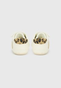 Scarpe per bambini bianche con un accento in stampa leopardata tan testurizzata sul tallone. Presentano una forma morbida e una chiusura in Velcro per una facile indossabilità.