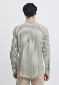 Camisa de manga larga a rayas en tonos de oliva claro y blanco, con cuello abotonado y dobladillo curvado, fabricada con un tejido texturizado.