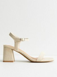 Beige tygklädd sandalett med blockklack, ankelrem och ett enkelt framband. Strukturerat material med en slät sula.