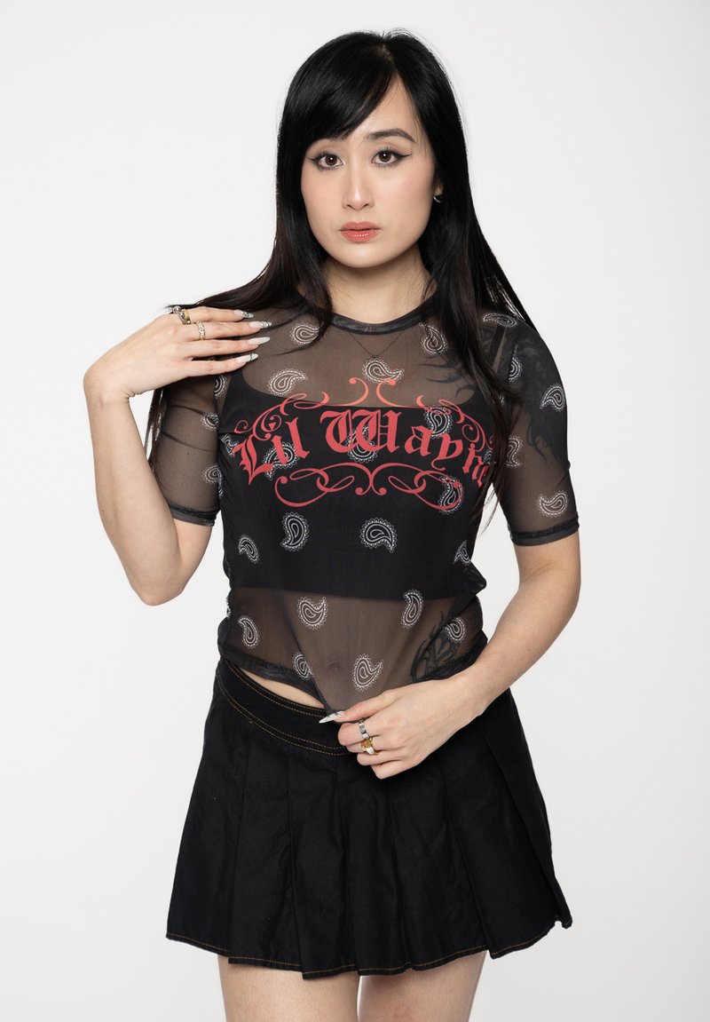 Black sheer mesh top with paisley patterns and red "Lil Wap" text; paired with a black pleated skirt. Features short sleeves and a fitted design.