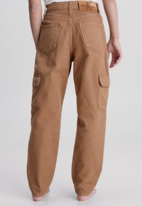 Braune Cargo-Hosen mit lockerer Passform. Sie verfügen über zwei Gesäßtaschen und eine Seitenasche, hergestellt aus robustem Stoff mit sichtbaren Nähten und Nähten.