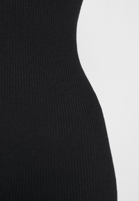 Gros plan sur un tissu tricoté côtelé noir montrant une silhouette ajustée sur un fond gris clair.