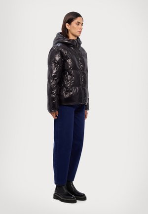 Black puffer jacket with a glossy finish, hood, and zip closure, worn with blue denim trousers and black ankle boots.