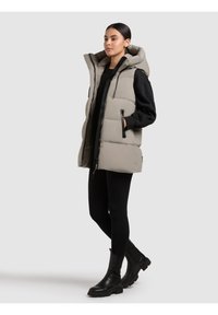 Helehall hall valles kerge hall vest kõrge kraega, lukuga ees ja mustade detailidega. Kombineeritud musta sviitriga ja retuusidega, viimistletud mustade saapadega.