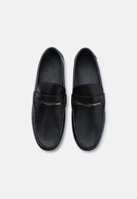 Sorte skinnloafers med sømdetaljer, sølvfarget hardware og flat såle. Glatt tekstur og minimalistisk design.