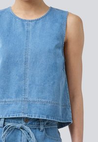 Light blue denim sleeveless top with a round neckline, cropped design, and visible stitching details; paired with matching denim bottoms.