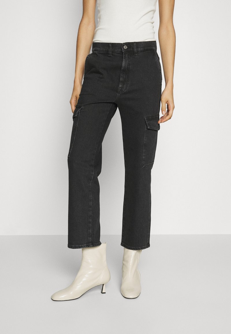 Zwarte denim cargobroek met een rechte pijp en zijzakken, gecombineerd met crèmekleurige enkellaarsjes. De stof heeft een gladde textuur.