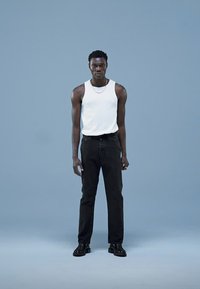 Valge varrukateta top, mustad teksad ja mustad kingad modellil helesinise tausta vastu. Lihtne disain, vormiv siluett.