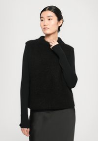 Svart ullblanding ermeløs topp med høy hals; strukturert overdel og rillet lange ermer; glatt stoff under, minimalistisk design.