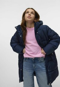 Granatowa kurtka puchowa z kapturem, z dodatkami w kolorze srebrnym. Nosi ją osoba na jasnoróżowym swetrze i niebieskich dżinsach, prezentując luzacką, warstwową stylizację.