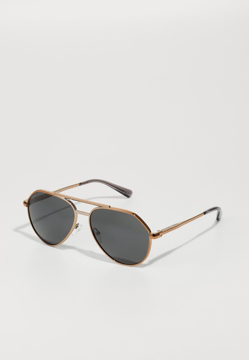 Óculos de sol estilo aviador com uma armação de metal dourado, lentes cinza-escuro e pontas de templo texturizadas em preto. Possui almofadas no nariz para maior conforto.