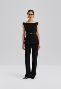 Čierny prispôsobený outfit pozostávajúci z vrchného dielu s odhalenými ramenami a nohavíc s širokými nohavicami, doplnený tenkým opaskom so zlatým detailom.