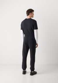 Black T-shirt with short sleeves and a round neckline; paired with dark joggers featuring a drawstring waist and elastic cuffs.
