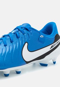 Botas de fútbol sintéticas azules con superficie texturizada, swoosh blanco de Nike, acentos negros y tacos azules para tracción. Cuenta con cierre de cordones.