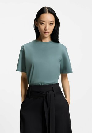 T-shirt met korte mouwen en ronde hals van zacht gedempt teal stof, met een gladde textuur, gecombineerd met hooggesloten zwarte broek met een strikdetail in de taille.