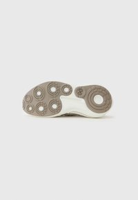 Shoe outsole in light brown with circular patterned treads and a white midsole. Features detailed grip points and brand logo.