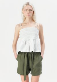 Fehér és kék csíkos peplum top, smockolt testrésszel és állítható pántokkal, lazán illeszkedő olajzöld rövidnadrággal, megkötős derékkal párosítva.