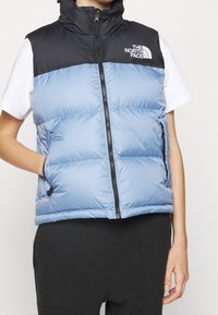 Pikowana kamizelka w jasnoniebieskim i czarnym kolorze, z wysokim kołnierzem, zamkiem błyskawicznym z przodu oraz bocznymi kieszeniami. Na piersi znajduje się logo oraz metka z oznaczeniem izolacji 700.