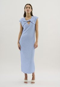 Rochie maxi texturată, de culoare albastru deschis, cu decolteu în V și detalii în formă de fundă; siluetă ajustată cu mâneci scurte, purtată cu pantofi cu vârf descoperit.